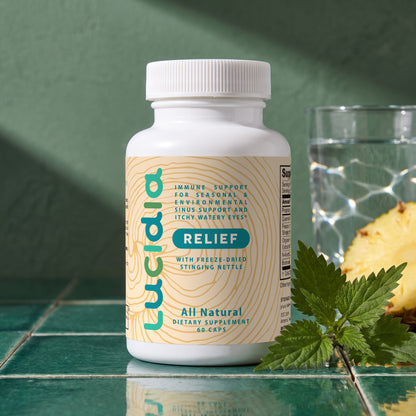 Lucidia Original bottle on green tiles in morning sun, with fresh nettle, pineapple and a glass of water