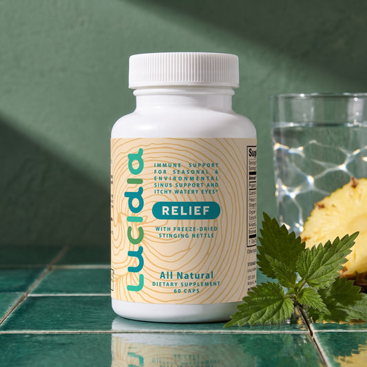 Lucidia Original bottle on green tiles in morning sun, with fresh nettle, pineapple and a glass of water