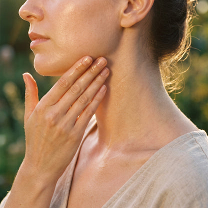 Fingertips smoothing oil along the jawline and neck at golden hour